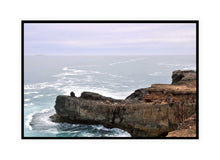 Load image into Gallery viewer, Ocean Photography Wall Art Print of the ocean gently kissing the rugged cliff ledge against a cloudy pink tinged sky. Canvas Print with Black Frame.
