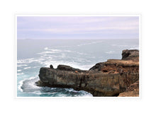 Load image into Gallery viewer, Ocean Photography Wall Art Print of the ocean gently kissing the rugged cliff ledge against a cloudy pink tinged sky. Canvas Print with White Frame.
