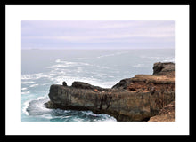 Load image into Gallery viewer, Ocean Photography Wall Art Print of the ocean gently kissing the rugged cliff ledge against a cloudy pink tinged sky. Fine Art Print with Black Frame. 
