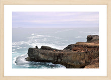 Load image into Gallery viewer, Ocean Photography Wall Art Print of the ocean gently kissing the rugged cliff ledge against a cloudy pink tinged sky. Fine Art Print with Wood Frame.
