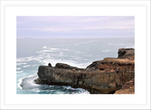 Load image into Gallery viewer, Ocean Photography Wall Art Print of the ocean gently kissing the rugged cliff ledge against a cloudy pink tinged sky. Fine Art Print with White Frame.
